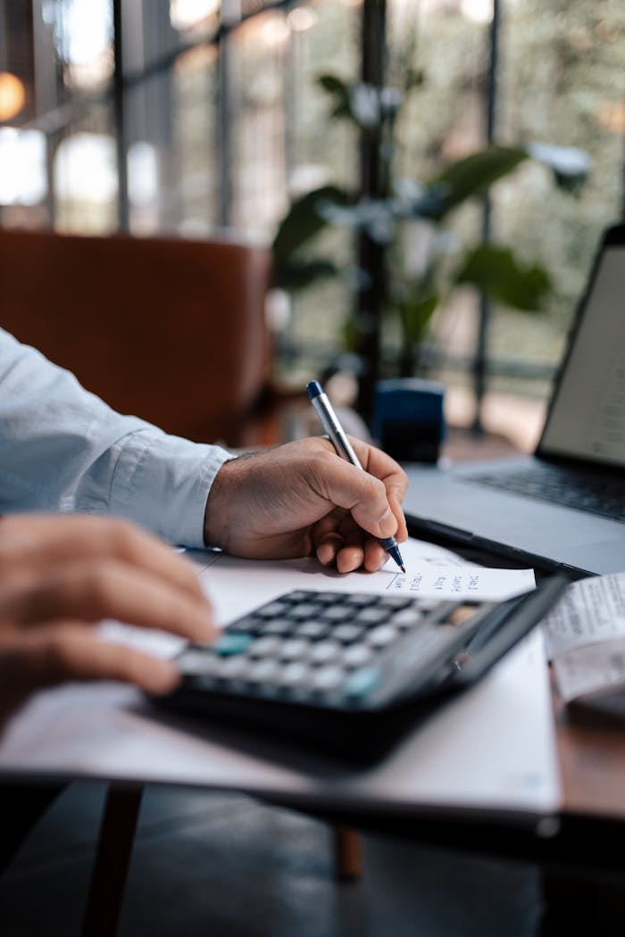 services-img A person calculating finances with a calculator and pen on a desk indoors.
