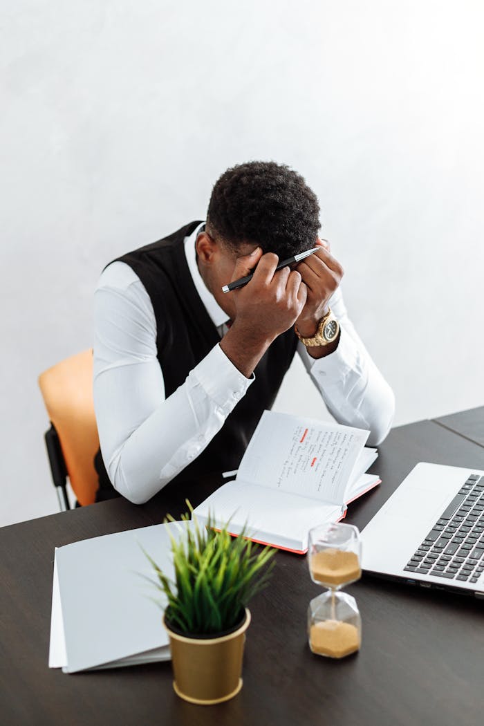 gallery-01 A businessman overwhelmed working indoors with a notebook, laptop, and hourglass.
