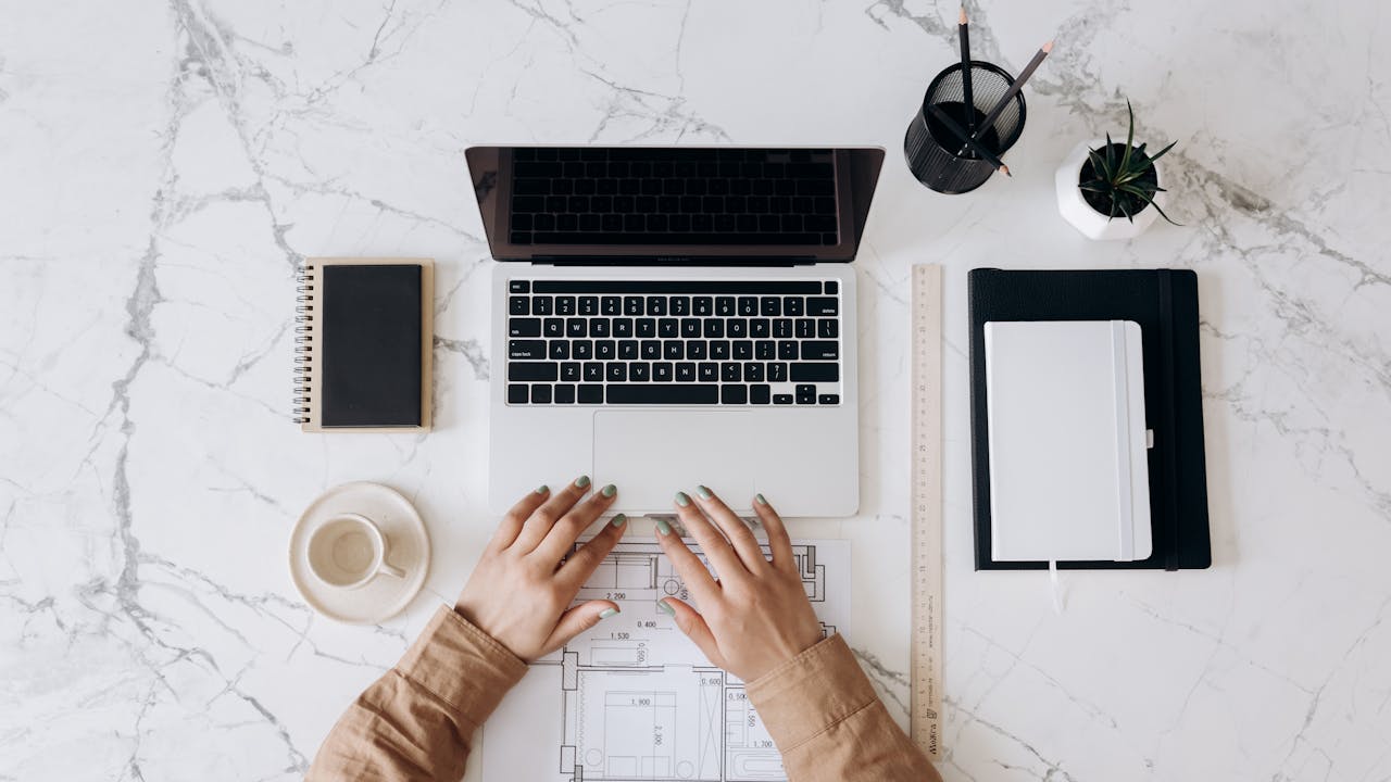 vision Top view of a stylish home office desk with a laptop, planner, and coffee cup, showing hands on a blueprint.